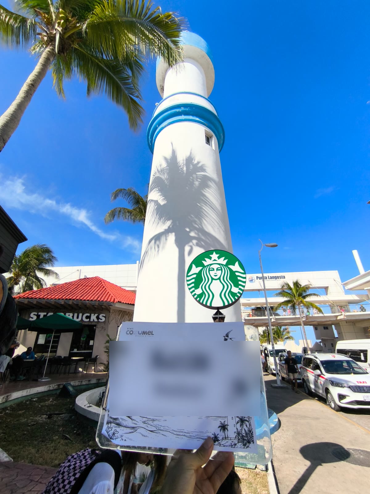 Our representative holding a Visit Cozumel Shuttles and Tours board under the white lighthouse, next to Starbucks at Punta Langosta